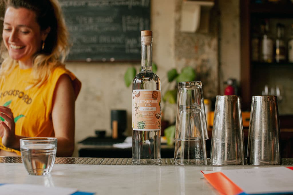Letherbee Gin Vernal bottle on a marble bar with glassware and service in the background.