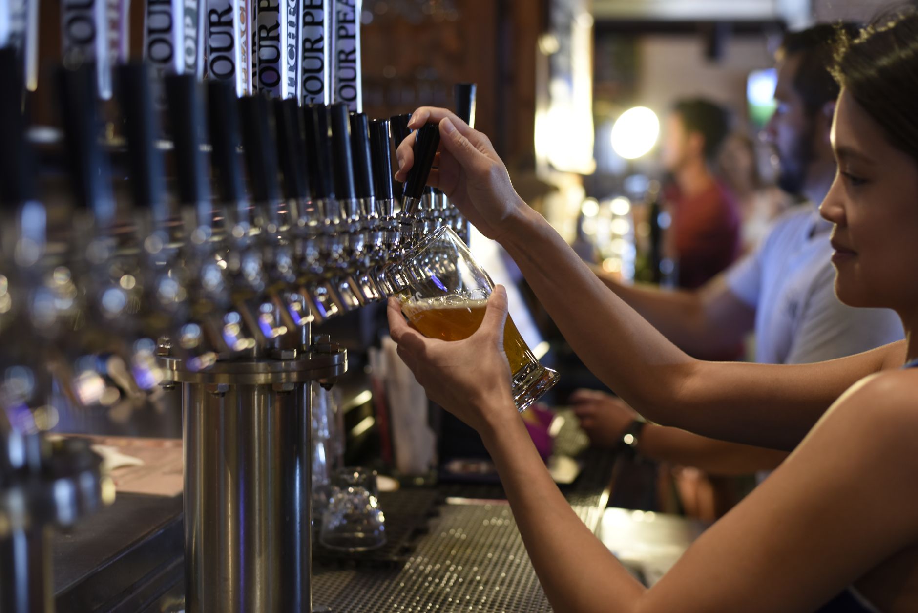 Female bartender pours craft beer in a lively pub setting. — Photo by ELEVATE on Pexels