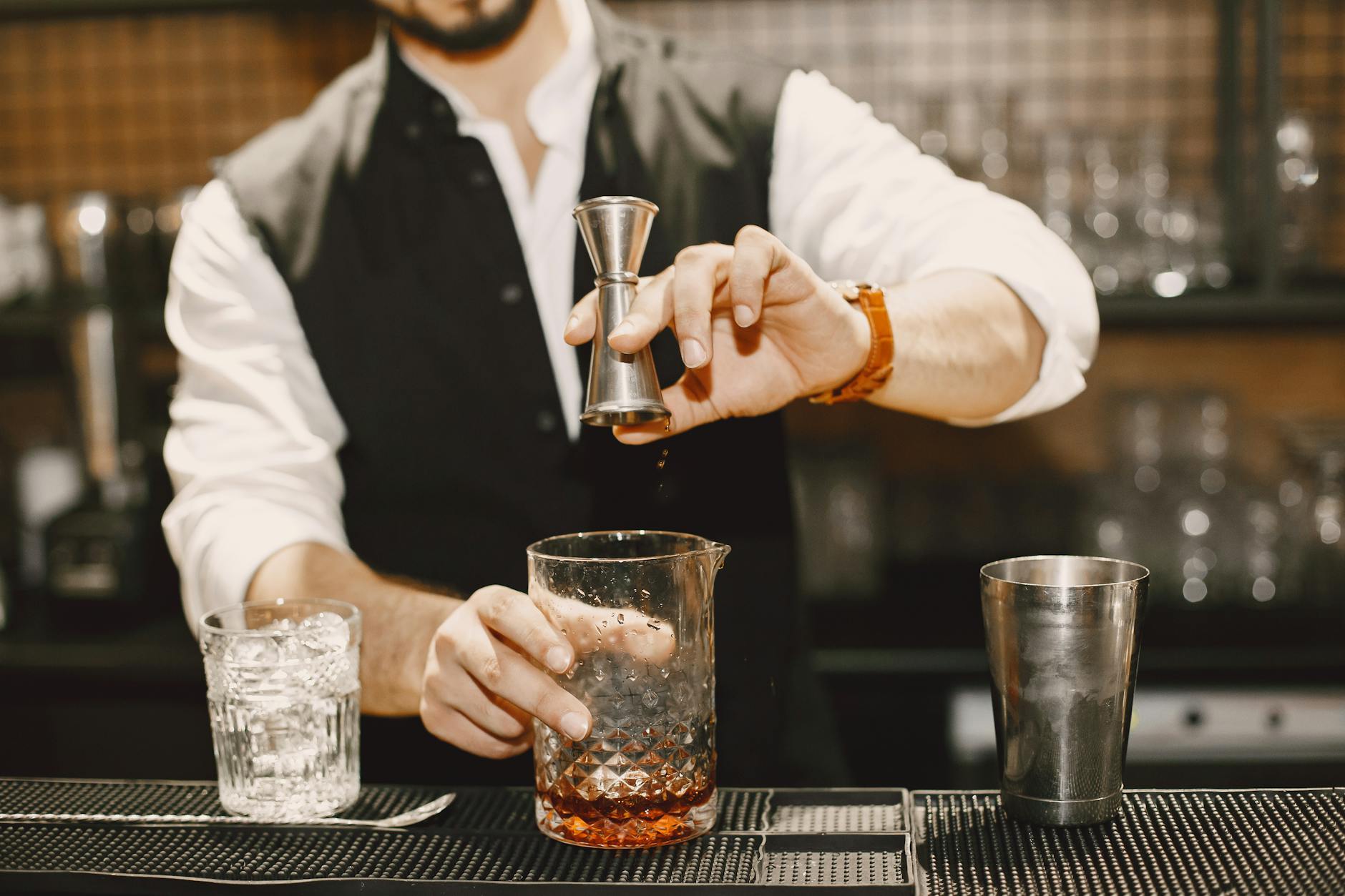 Bartender preparing a cocktail using a jigger and mixing glass at an elegant bar. — Photo by Gustavo Fring on Pexels